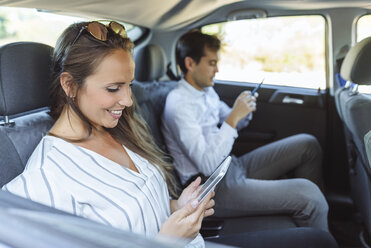 Frau und Mann benutzen Tablet und Handy auf dem Rücksitz eines Autos - KIJF02108