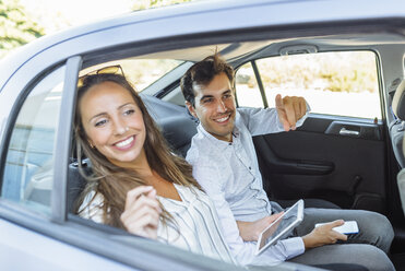 Lächelndes Paar auf dem Rücksitz eines Autos, das aus dem Fenster schaut - KIJF02109