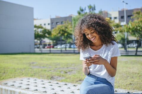 Smiling young woman sitting on bench text messaging stock photo