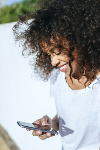 Lächelnde junge Frau schaut auf ihr Handy, lizenzfreies Stockfoto