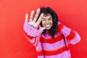 Porträt einer lachenden jungen Frau vor einer roten Wand - KIJF02125