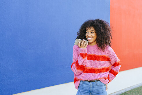 Portrait of smiling young woman sending a voice message with mobile phone - KIJF02129