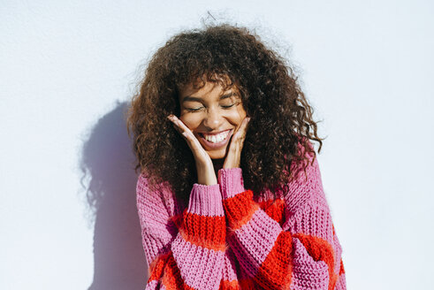 Portrait of laughing young woman with curly hair against white wall - KIJF02132