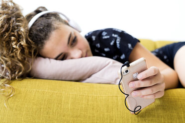 Girl lying on the couch at home listening music with headphones and smartphone - ERRF00053