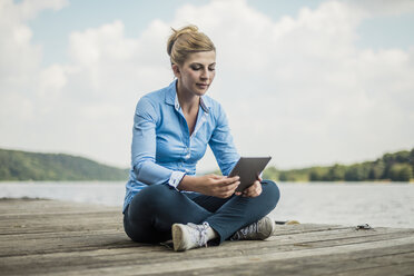 Frau sitzt auf einem Steg an einem See und benutzt ein Tablet - MOEF01488