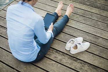 Woman sitting on jetty at a lake using tablet - MOEF01489