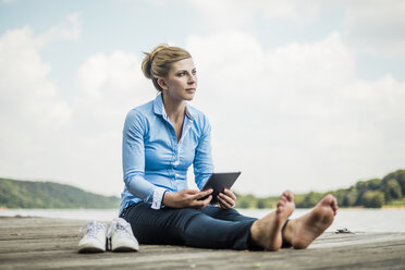 Woman sitting on jetty at a lake using tablet - MOEF01491