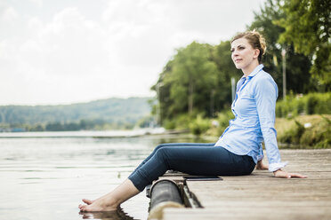 Frau sitzt auf einem Steg an einem See mit den Füßen im Wasser - MOEF01493