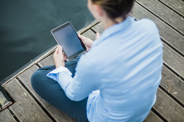 Frau sitzt auf einem Steg an einem See und benutzt ein Tablet - MOEF01494