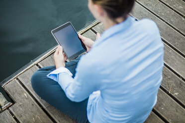 Woman sitting on jetty at a lake using tablet - MOEF01494