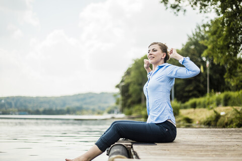 Frau sitzt auf einem Steg an einem See mit den Füßen im Wasser, lizenzfreies Stockfoto
