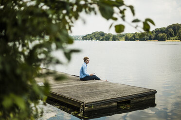 Frau sitzt auf einem Steg an einem See und entspannt sich - MOEF01498