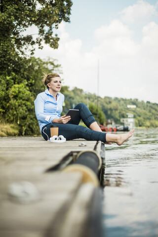 Woman sitting on jetty at a lake with tablet stock photo