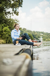 Frau auf Steg an einem See mit Tablet sitzend - MOEF01507