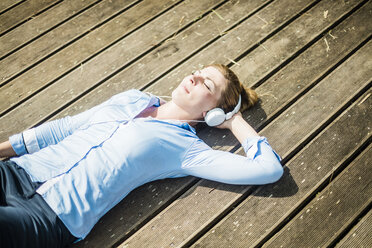 Woman lying on planks wearing headphones - MOEF01513