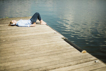 Woman lying on jetty at a lake with headphones and takeaway coffee - MOEF01516