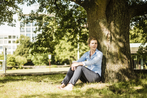 Frau sitzt im Stadtpark und lehnt sich an einen Baum, lizenzfreies Stockfoto