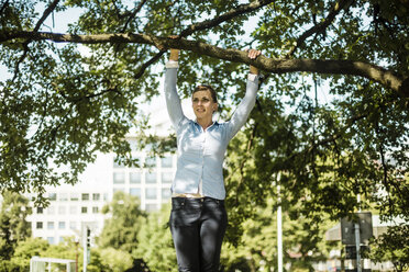 Woman in urban park hanging at branch of a tree - MOEF01523