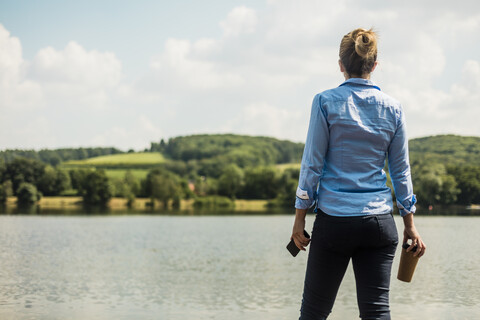 Woman standing at a lake with cell phone and takeaway coffee stock photo