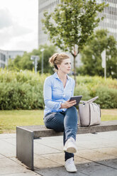 Woman sitting on a bench holding tablet - MOEF01530