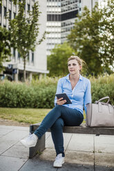 Woman sitting on a bench holding tablet - MOEF01532