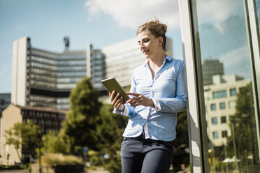 Smiling woman leaning against a building using tablet - MOEF01549