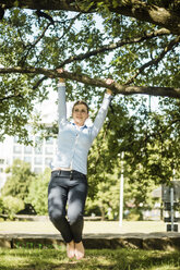 Frau im Stadtpark am Ast eines Baumes hängend - MOEF01553