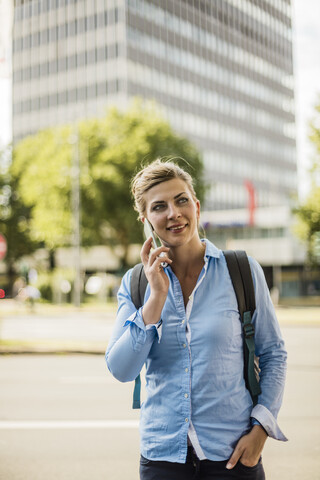 Lächelnde Frau mit Rucksack in der Stadt im Gespräch mit dem Handy, lizenzfreies Stockfoto