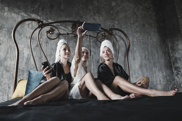 Drei Frauen mit Handtüchern um ihre Köpfe auf dem Bett machen ein Selfie - KMKF00632