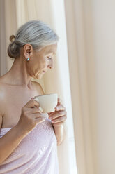 Ältere Frau, eingewickelt in ein Handtuch, trinkt eine Tasse Kaffee am Morgen - VGF00109