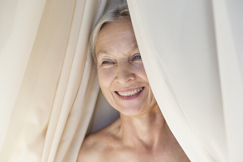 Porträt einer entspannten älteren Frau hinter einem Vorhang, lizenzfreies Stockfoto