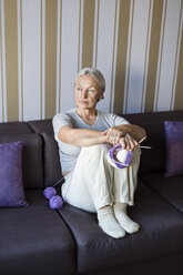 Portrait of pensive senior woman sitting on the couch with knitting looking at distance - VGF00116