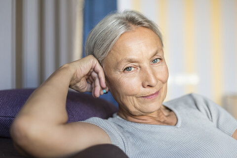 Porträt einer lächelnden älteren Frau, die sich zu Hause auf der Couch entspannt, lizenzfreies Stockfoto