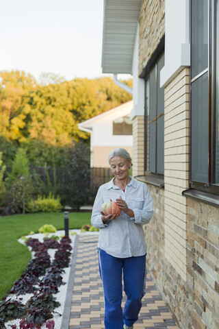 Lächelnde Seniorin mit geerntetem Kürbis im Garten, lizenzfreies Stockfoto