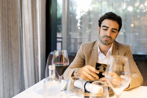 Mann sitzt am Tisch in einem Restaurant und benutzt ein Mobiltelefon, lizenzfreies Stockfoto