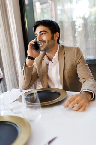 Lächelnder Mann, der an einem Tisch in einem Restaurant sitzt und mit einem Handy telefoniert, lizenzfreies Stockfoto