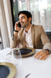 Lächelnder Mann, der an einem Tisch in einem Restaurant sitzt und mit einem Handy telefoniert - VABF01644