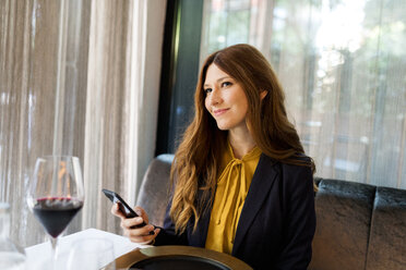 Lächelnde Frau sitzt am Tisch in einem Restaurant und hält ein Handy in der Hand - VABF01649