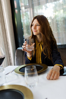 Lächelnde Frau sitzt am Tisch in einem Restaurant und trinkt ein Glas Wasser - VABF01652