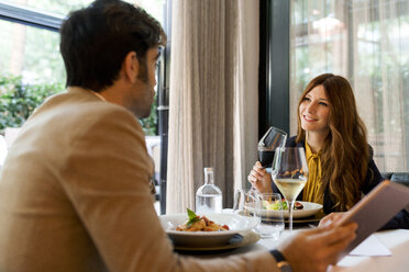 Lächelnde Frau mit einem Glas Rotwein, die einen Mann in einem Restaurant ansieht - VABF01655
