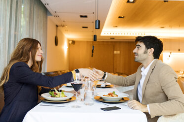 Smiling man and woman shaking hands in a restaurant - VABF01657