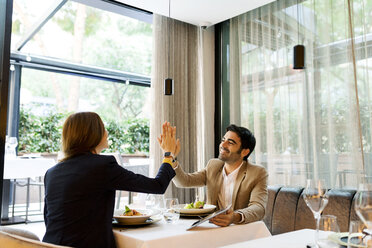 Happy man and woman with a tablet in a restaurant high fiving - VABF01661
