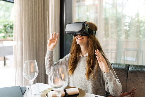 Frau sitzt am Tisch in einem Restaurant und trägt eine VR-Brille, lizenzfreies Stockfoto