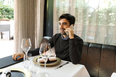 Mann sitzt am Tisch in einem Restaurant und spricht mit seinem Handy - VABF01680