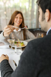 Smiling woman letting man taste the food in a restaurant - VABF01686