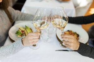 Nahaufnahme eines Paares, das in einem Restaurant mit Weingläsern anstößt - VABF01692
