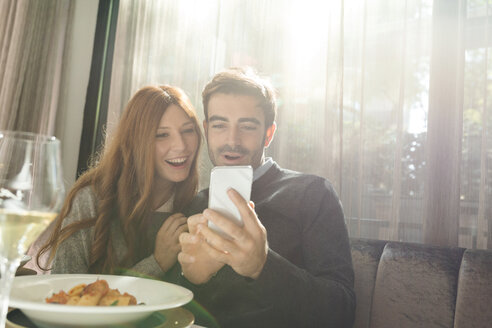 Glückliches Paar schaut in einem Restaurant auf sein Handy - VABF01696
