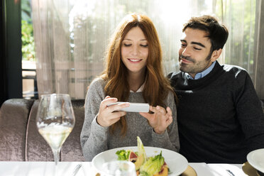 Lächelndes Paar benutzt Handy in einem Restaurant - VABF01700