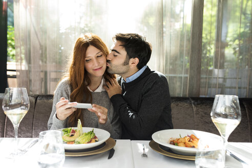 Mann küsst Frau, die ein Handyfoto in einem Restaurant macht - VABF01701