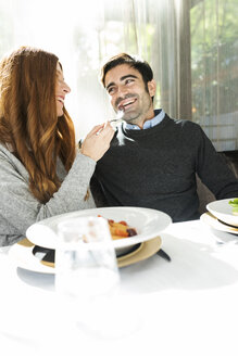 Smiling woman letting man taste the food in a restaurant - VABF01702